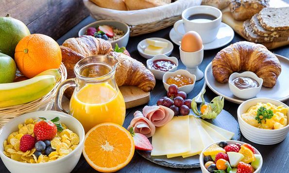 Frühstukstisch mit Tee und Kaffee, frischen Brötchen, Wurst, Schinken, Käse, Butter, Marmelade, Kuchen, Orangensaft, Müsli, Honig, Nutella, Leberaufstrich und Cornflakes.